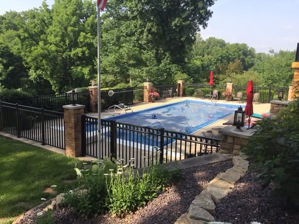 Black aluminum pool fence with brick pillars around an inground pool