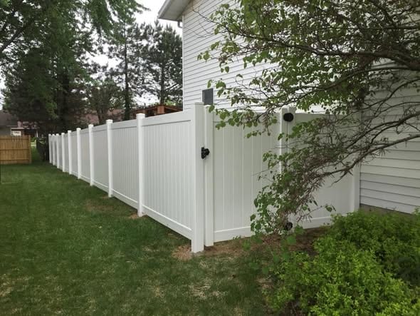 White vinyl privacy fence and walk gate alongside a home