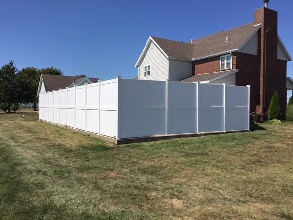 Tall white vinyl privacy fence at a two-story brick home